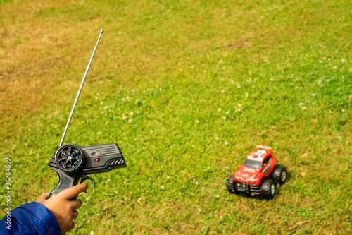The child's hand holds the remote control of the radio-controlled model.Against the background of green grass and a red car in a blur.