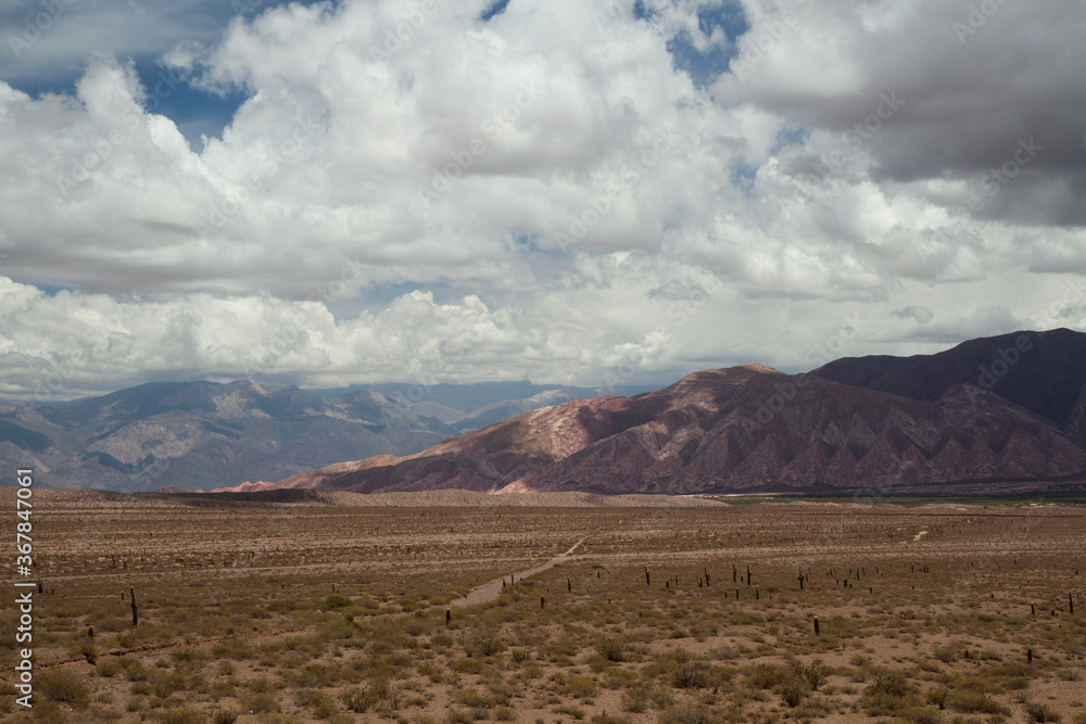 Travel. Dirt road across the arid desert and into the mountains under a cloudy sky.	
