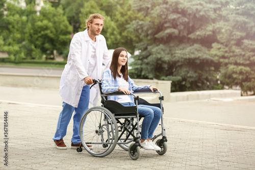 Doctor and young woman in wheelchair outdoors