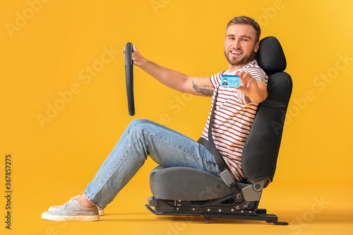 Young man with steering wheel and driving license sitting on car seat against color background photo