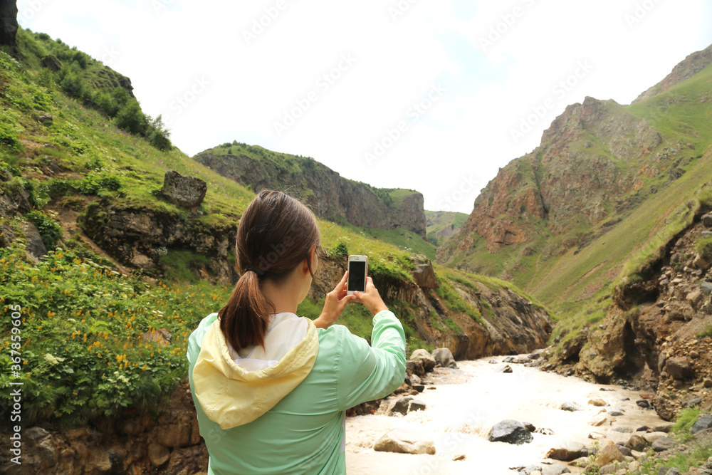 Young woman traveller taking photo in the mountains in Caucasus Russia. Freedom lifestyle.