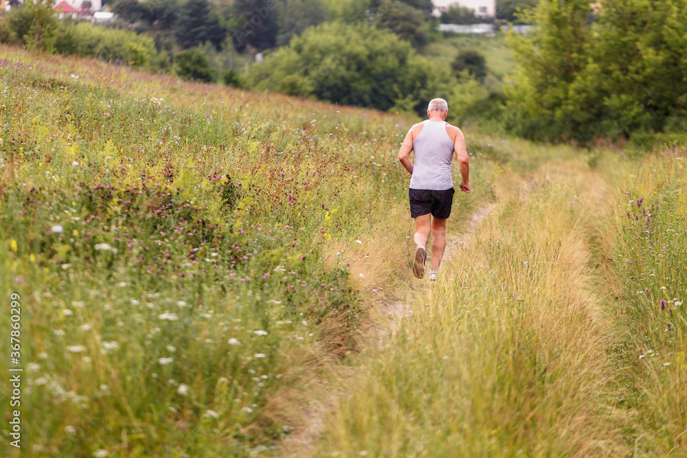 Elderly man runs along a flowering field outside the city Elderly man runs along a flowering field outside the city
