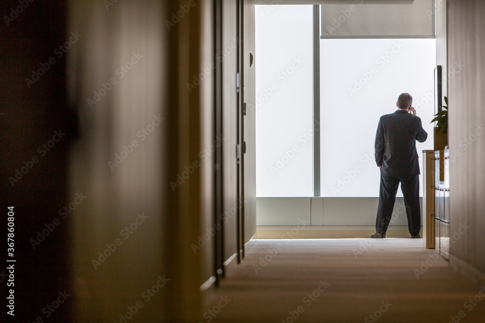 Rear view of businessman talking on phone while standing in corridor at office Rear view of businessman talking on phone while standing in corridor at office