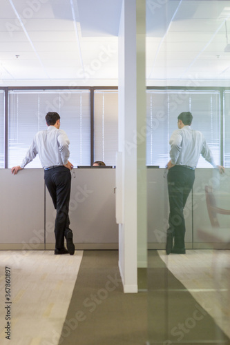 Rear view of businessman talking to colleague at cubicle against window in office