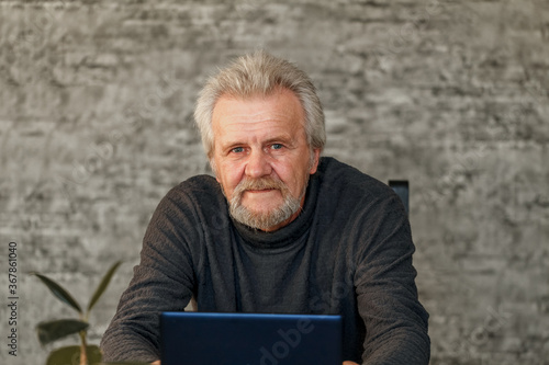 Elderly man uses Laptop in studio on brick wall background photo