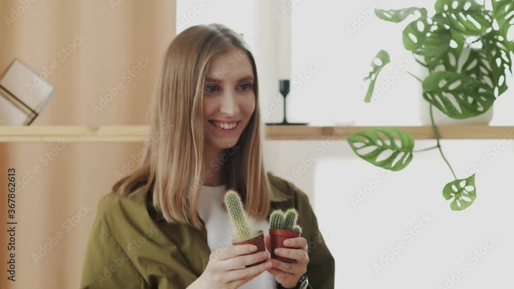 Young female gardener smiles and posing on camera with her favorite little cactuses in hands. Young female gardener smiles and posing on camera with her favorite little cactuses in hands.