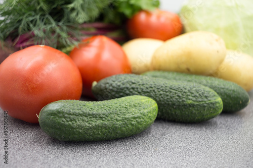 Fresh vegetables on a gray worktop, closeup: Potatoes, green onions, dill, tomato, parsley. Healthy food, vegan food.