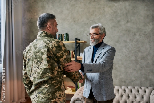 Wish you better life. Mature psychologist smiling, shaking hands with middle aged military man after therapy session. Soldier suffering from depression, psychological trauma. PTSD concept