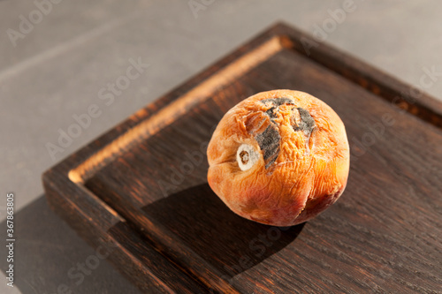 Spoiled, wrinkled peach on a dark wood cutting board. Close-up, selective focus. Rotten fruit. Incorrect storage of food photo