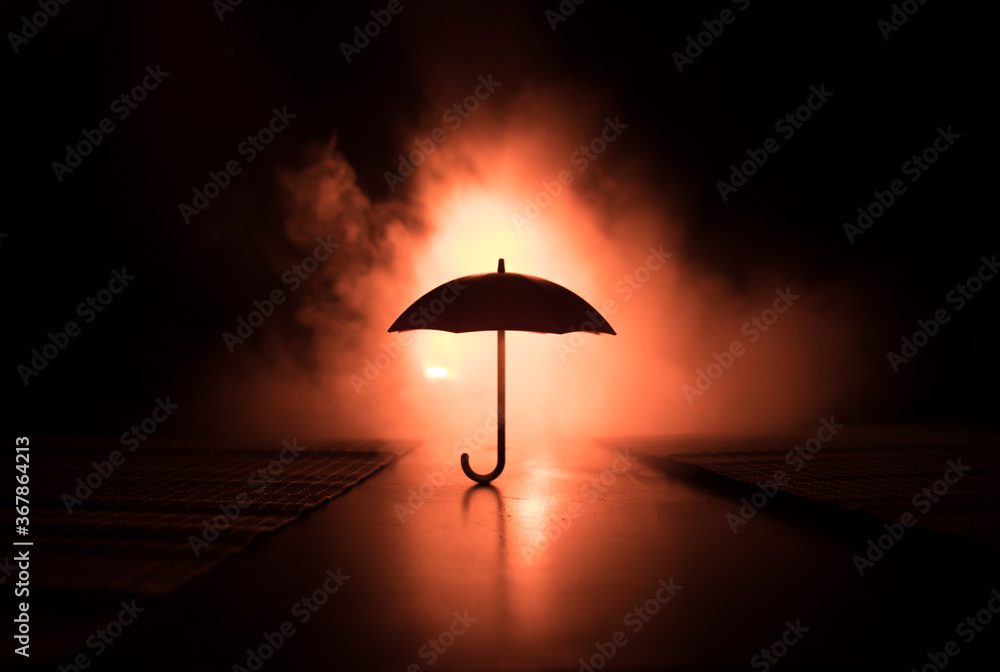 Silhouette of umbrella miniature on table with dark toned foggy background. Creative concept. Silhouette of umbrella miniature on table with dark toned foggy background. Creative concept.