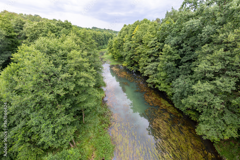A small river seen from the railway bridge. The river bed is covered with deciduous trees. A small river seen from the railway bridge. The river bed is covered with deciduous trees.