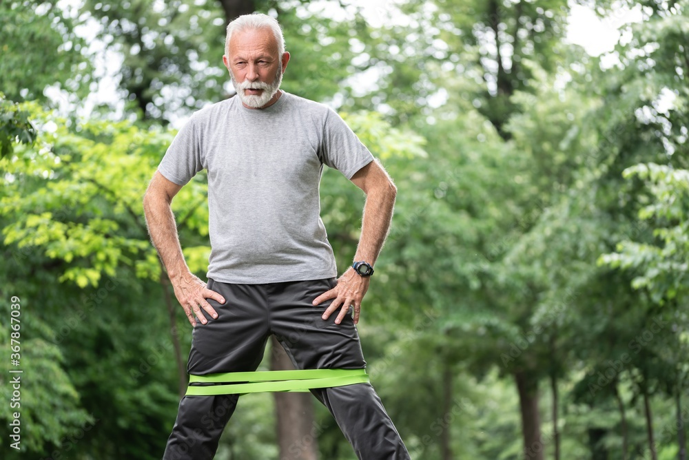 Senior sportsman exercising for glutes using resistance band at park Senior sportsman exercising for glutes using resistance band at park