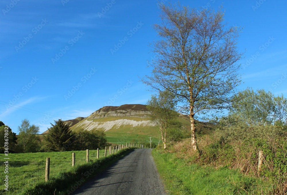 Rural road leading towards Keelogyboy mountain in Calry, County Sligo, Ireland, during springtime featuring blue sky