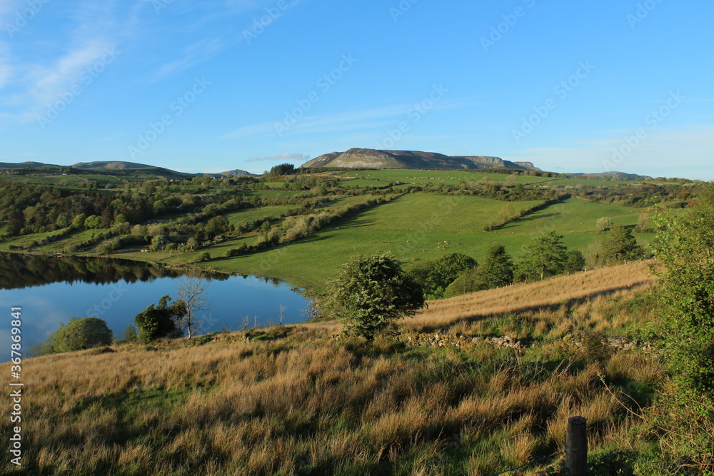 Landscape at Lough Colgagh, County Sligo, Ireland featuring still water lake, rolling hills of farmland and blue skies with clouds