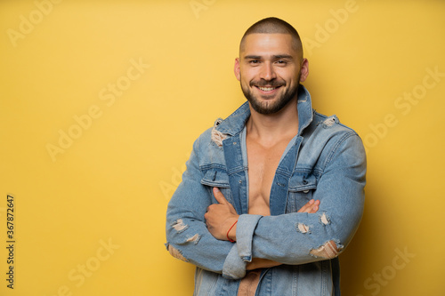 a smiling man with a naked body with a black beard and a fashionable barbershop haircut is photographed in a photo Studio, with a blue denim jacket thrown over the top © muse studio