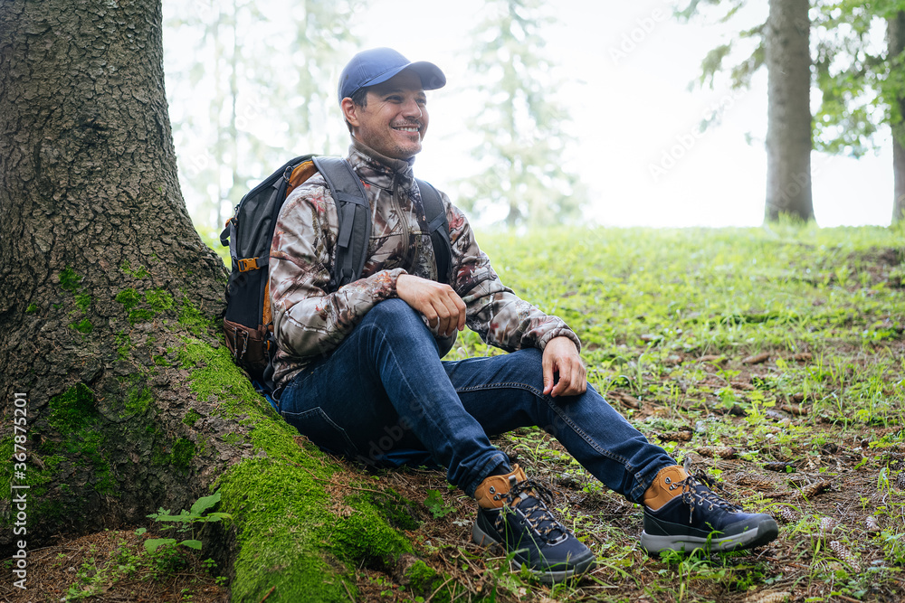 Man with backpack resting in forest after hiking on mountain Man with backpack resting in forest after hiking on mountain
