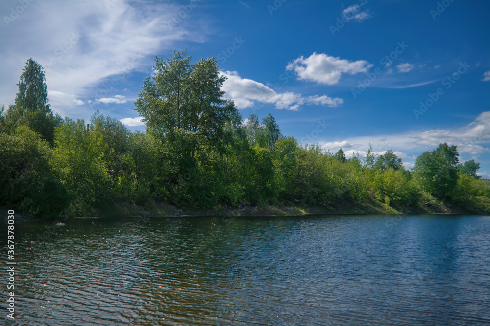 Beautiful summer landscape, forest trees are reflected in calm river water against a background of blue sky. Beautiful summer landscape, forest trees are reflected in calm river water against a background of blue sky.