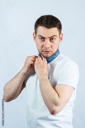 A man fastens a button on his white polo. he is on a white background. The guy is putting on a T-shirt. Facial expressions on a man's face