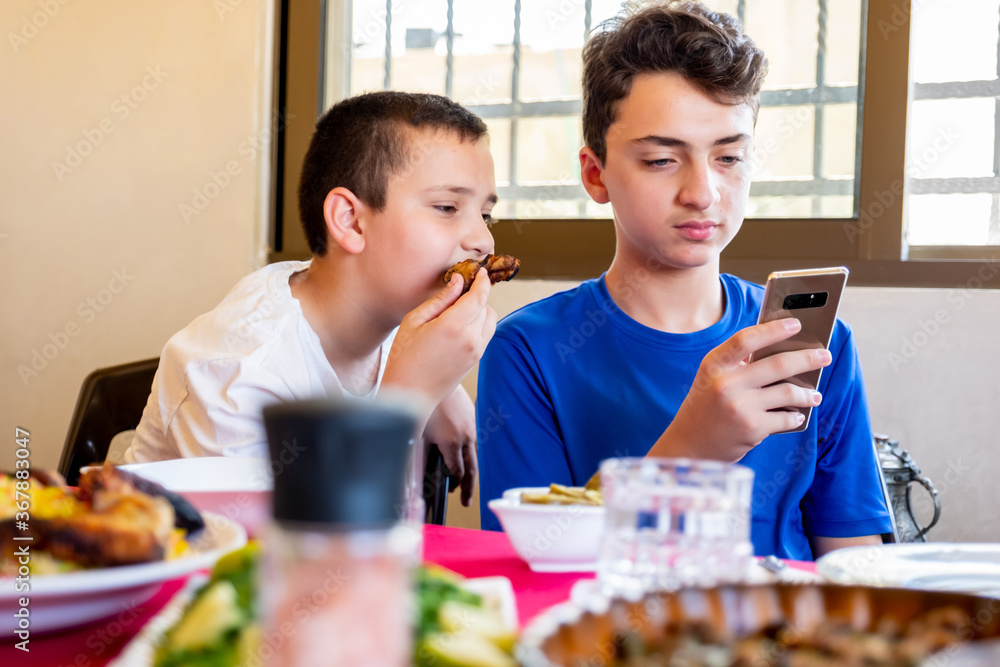 Arabic Muslim boys using their smartphones while eating 