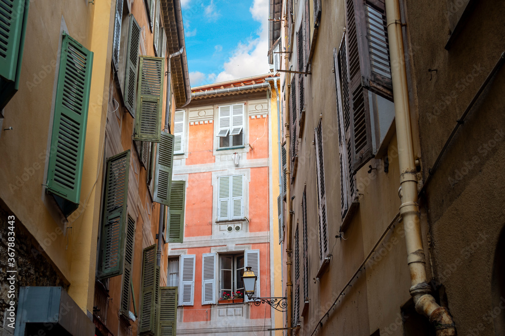 A colorful, historic apartment building under a blue sky is seen on a narrow street in old town Vieux Nice, France.
