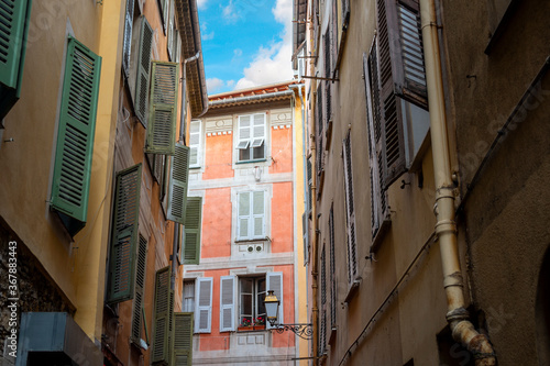 A colorful, historic apartment building under a blue sky is seen on a narrow street in old town Vieux Nice, France.