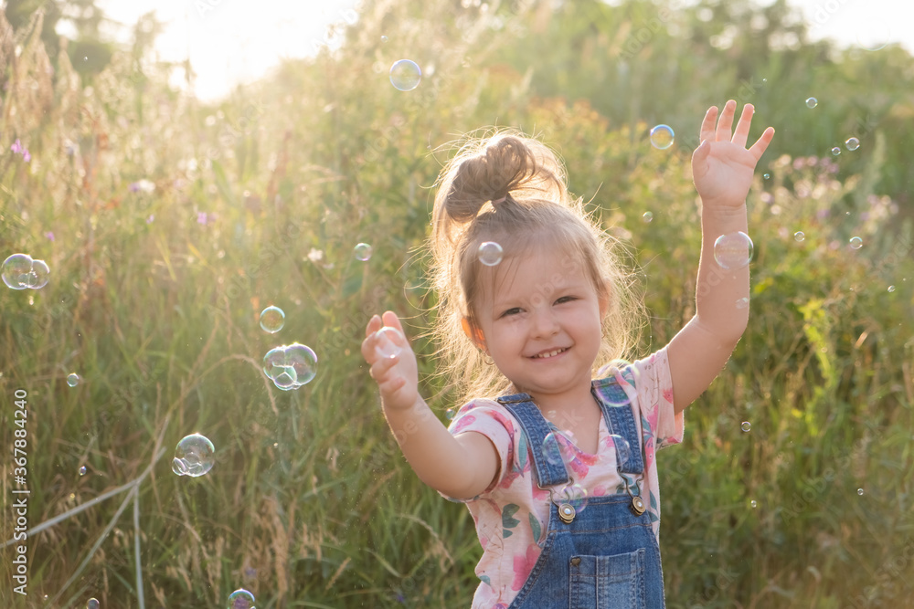 selective focus of little cute girl laughs playing with soap bubbles in nature.