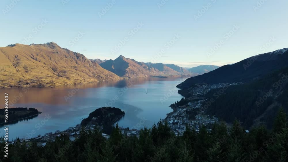 Scenic flight above dark tree forest to reveal Queenstown towards Lake Wakatipu and Remarkables mountain range, New Zealand, overhead aerial approach tilt down Scenic flight above dark tree forest to reveal Queenstown towards Lake Wakatipu and Remarkables mountain range, New Zealand, overhead aerial approach tilt down