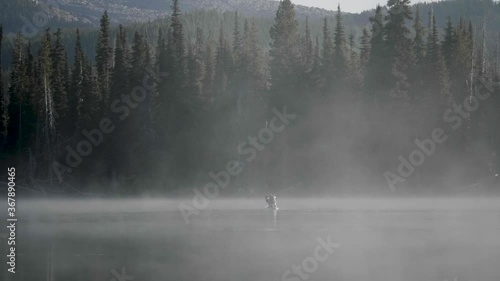 person with dog on kayak paddle across through misty fog covered water lake with forest trees and mountains background peaceful morning sparks lake central oregon usa slow motion
