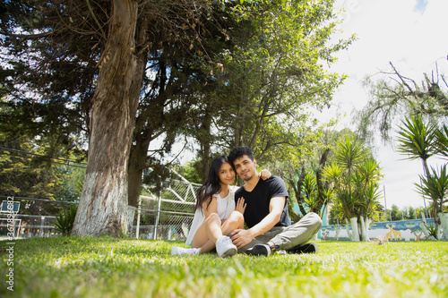 Young Hispanic couple in love sitting on the grass hugging and having fun - couple strolling in a natural park on a sunny day © Fernanda