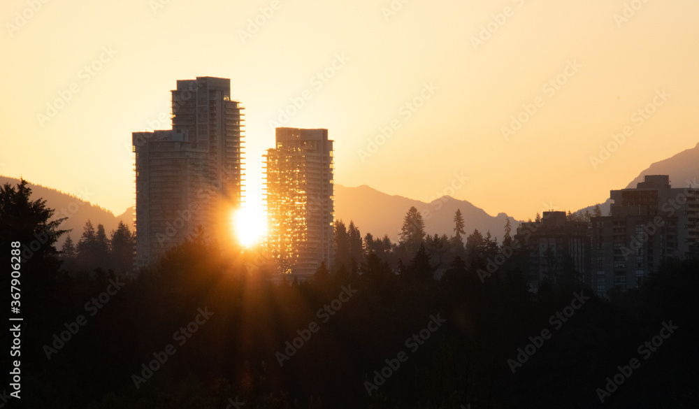 The orange-coloured sun peeking out from between two high rise buildings.   Vancouver BC Canada
