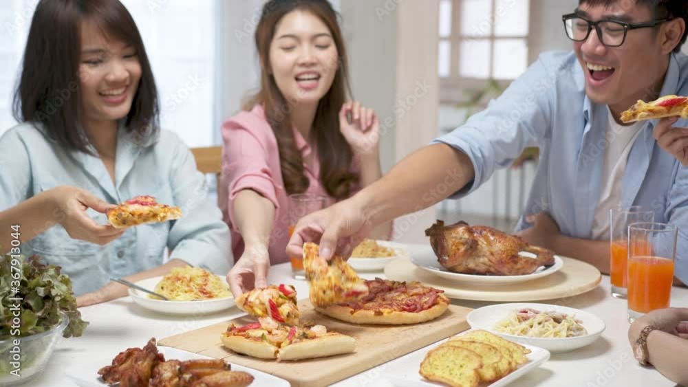 Medium shot happy asian friend eating pizza at home. Group friend cheerful mates laughing enjoying meal having fun sitting together at home dining table, diverse friends share lunch at meeting Medium shot happy asian friend eating pizza at home. Group friend cheerful mates laughing enjoying meal having fun sitting together at home dining table, diverse friends share lunch at meeting