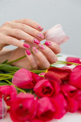 Close up vertical shot of woman hands with spring manicure holding pink tulip on tulips bouquet background. Nail art, gel nail polish design concept.