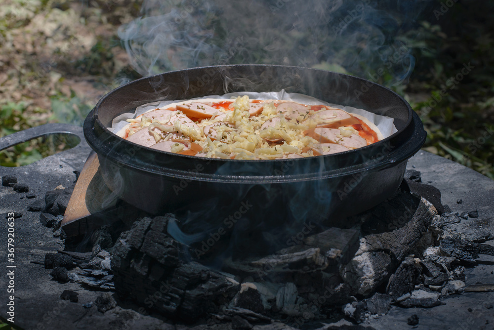 Cooking dinner pizza in camp oven over hot coals in the forest,Outdoor cooking. Cooking dinner pizza in camp oven over hot coals in the forest,Outdoor cooking.