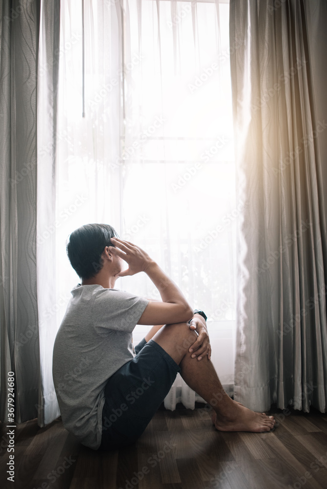 Sad and depressed young male sitting on the floor in the living room looking outside the doors,sad mood,feel tired, lonely and unhappy concept. Selective focus. Sad and depressed young male sitting on the floor in the living room looking outside the doors,sad mood,feel tired, lonely and unhappy concept. Selective focus.