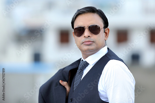 Young Indian confident businessman wearing suit and sunglasses standing outdoors.Young urban stylish professional looking confidently into viewers eyes.