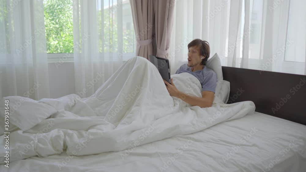 A young man in a bed has an argument with someone through video conferencing. He is tired of sitting at home during social isolation A young man in a bed has an argument with someone through video conferencing. He is tired of sitting at home during social isolation