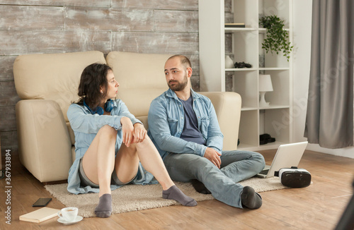 Couple looking at each other sitting down living room carpet. © DC Studio
