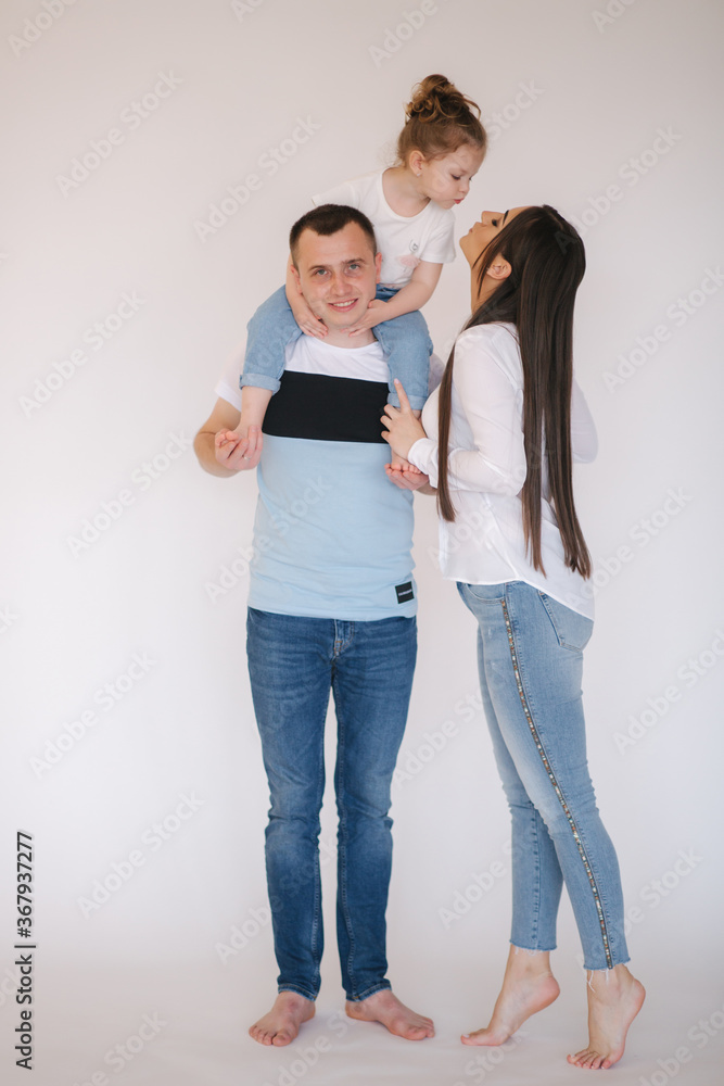 Adorable little girl sits on dad's neck. Mom kiss daughter Adorable little girl sits on dad's neck. Mom kiss daughter