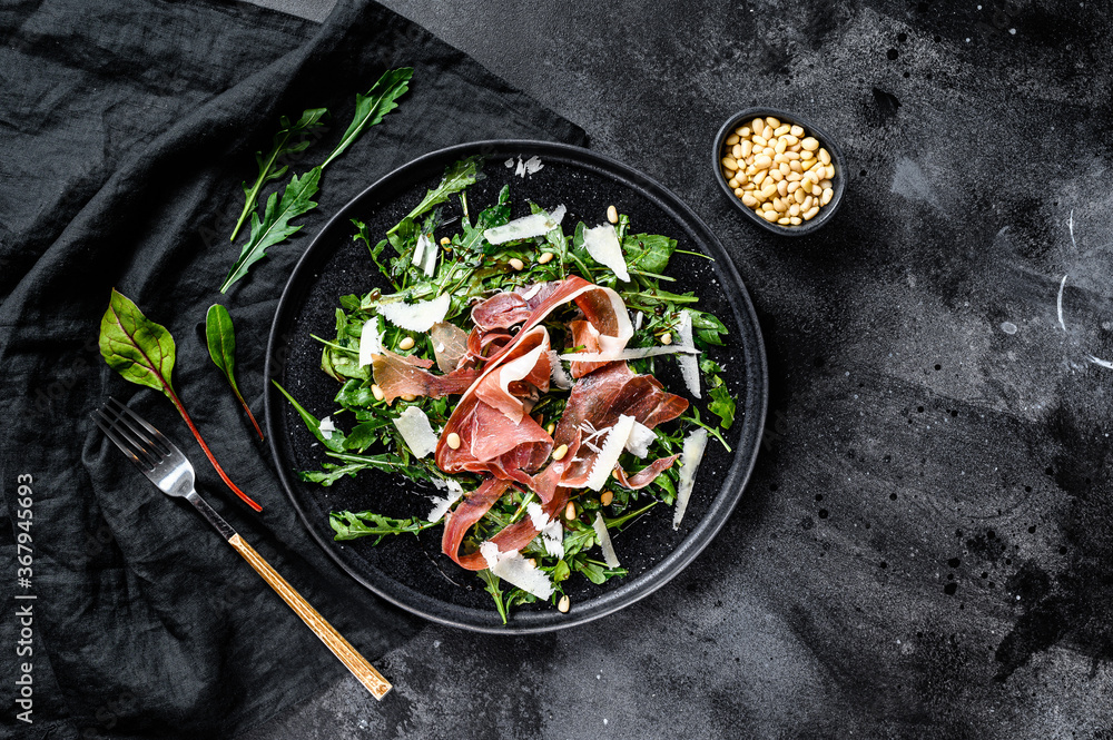 Salad with Serrano jamon, ham, rucola and Parmesan cheese. Black background, top view.
