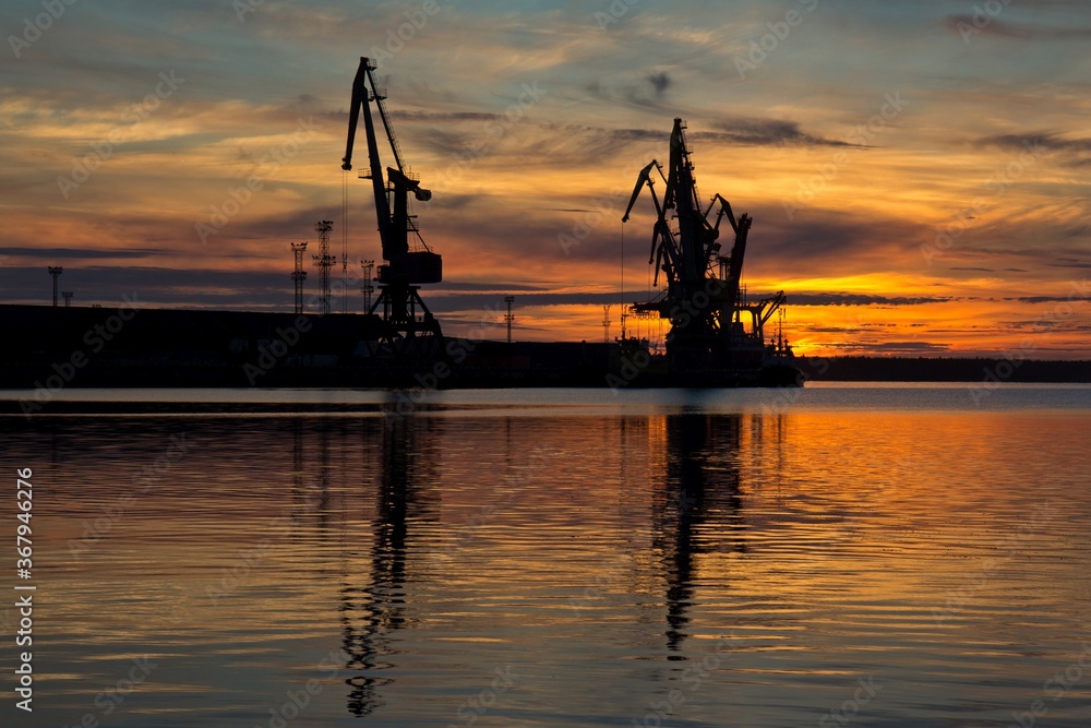 Black silhouettes of high cranes in sea cargo port and wonderful sunset. Arkhangelsk, Russia.