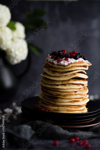 Stack of pancakes with sugar powder splashes on dark background table.