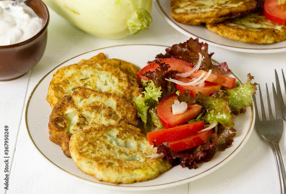 Zucchini fritters with tomato salad on a white background Zucchini fritters with tomato salad on a white background