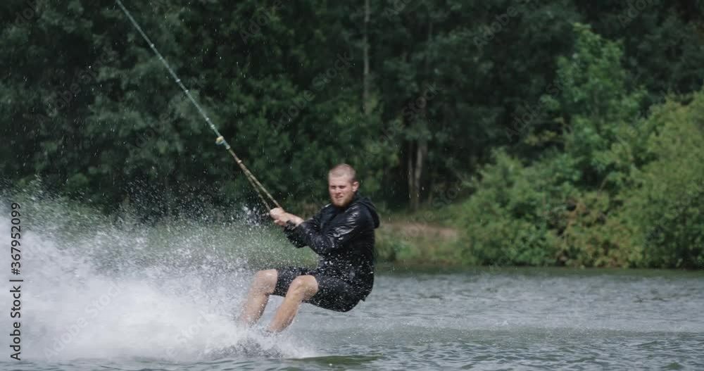 Wakeboarding in a lake near the forest, sportsman surfs on the water, ride on a wakeboarding board, performs tricks and does a somersault, 4k slow motion. Wakeboarding in a lake near the forest, sportsman surfs on the water, ride on a wakeboarding board, performs tricks and does a somersault, 4k slow motion.