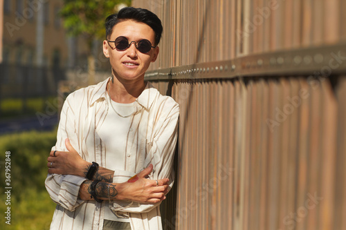 Portrait of young woman with dark short hair wearing sunglasses smiling at camera while standing outdoors photo