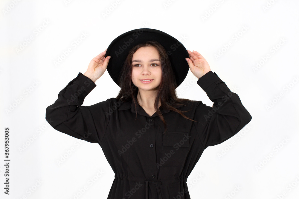 A girl in a black hat poses and smiles on a white background A girl in a black hat poses and smiles on a white background