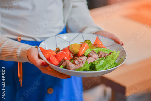 Waiter serves roasted meat and vegetables salad with tomatoes and brocolli in a white bowl. Eating out in restaurant.