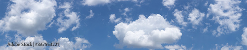 Panorama of diffuse white, puffy clouds against a clear blue sky background, creative copy space, horizontal aspect