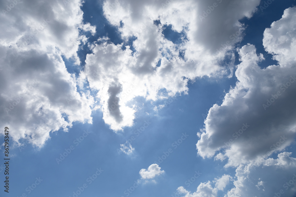 View directly overhead of sun peaking through white and gray clouds, blue sky beyond, creative bbackground copy space, horizontal aspect View directly overhead of sun peaking through white and gray clouds, blue sky beyond, creative bbackground copy space, horizontal aspect