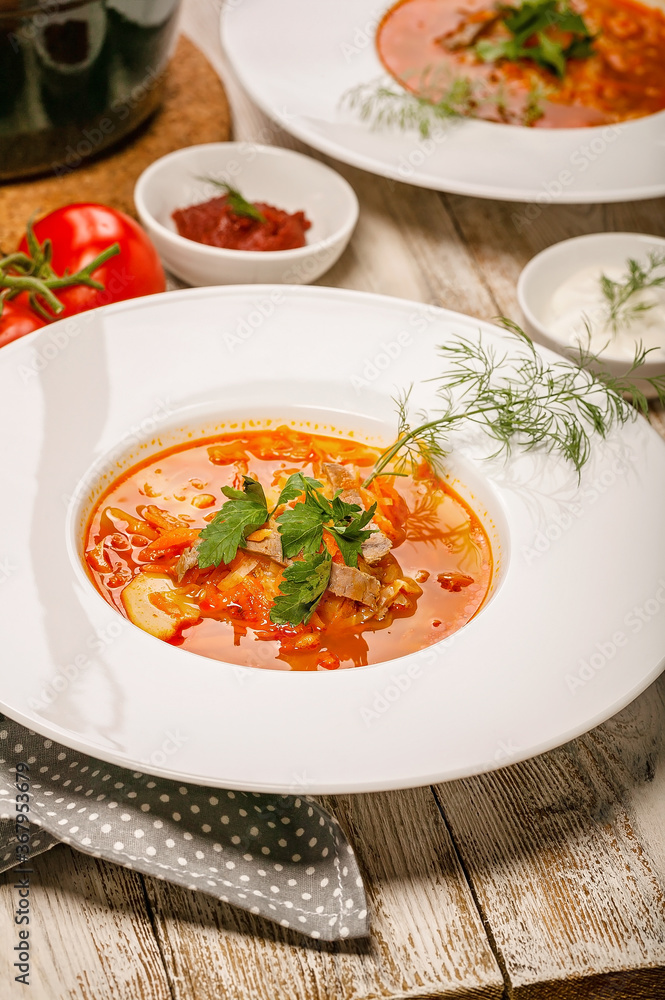 Close-up plate cabbage soup with beef, fresh tomatoes and herbs on a light wooden background. Vertical shot Close-up plate cabbage soup with beef, fresh tomatoes and herbs on a light wooden background. Vertical shot