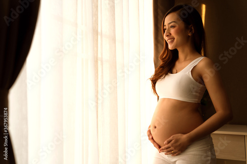 a beautiful woman pregnant in standing beside windows smiley happy and relax in bed room her Free Download a beautiful woman pregnant in standing beside windows smiley happy and relax in bed room her - GFXLoad